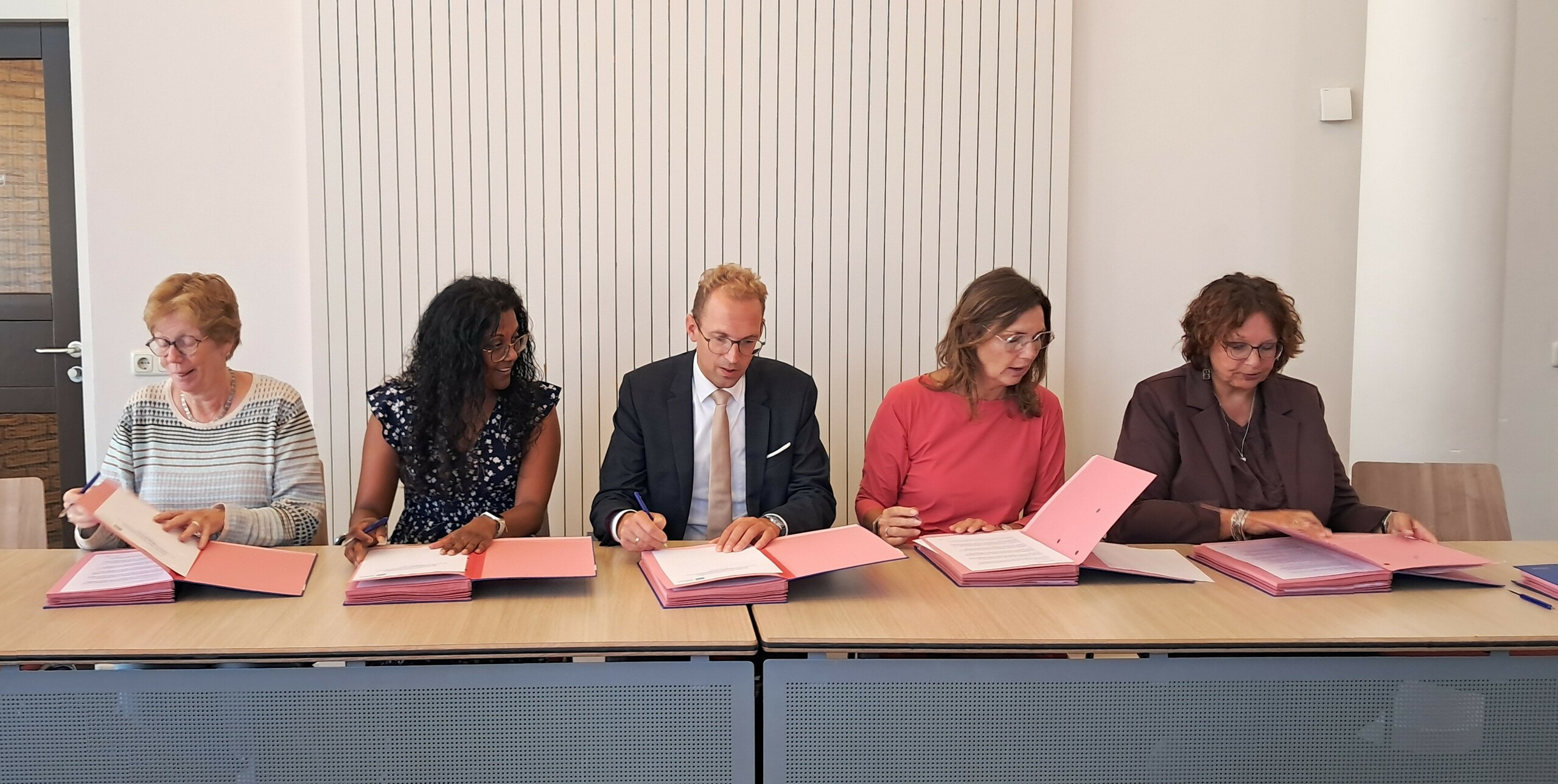 Vertegenwoordigers partijen zitten aan een tafel en ondertekenen de overeenkomst.